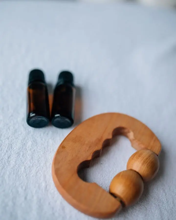 Close-up of essential oil bottles and a wooden massager on a soft surface.