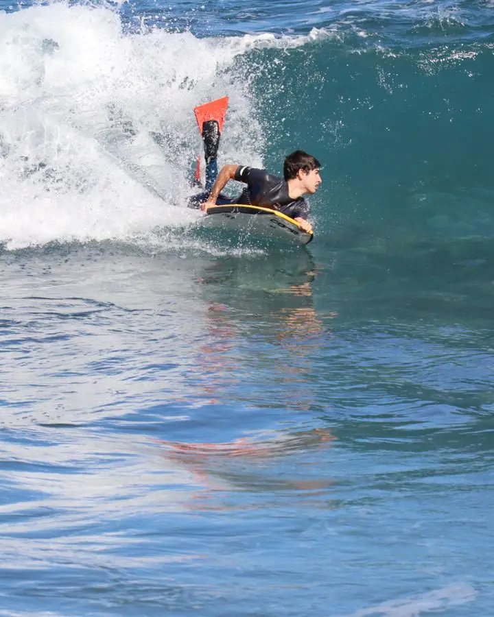 An energetic young man bodyboarding a wave in the bright ocean waters, showcasing extreme water sports.