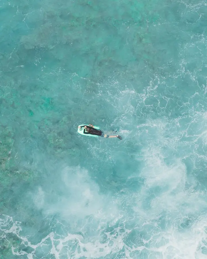 Drone photo of a surfer with bodyboard in the vibrant turquoise waters of Hawaii, showcasing ocean waves.