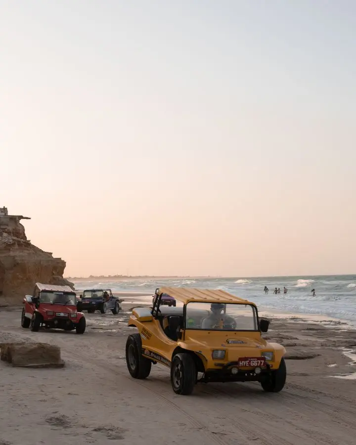 Yellow buggy cars drive along a sandy beach, capturing an adventurous spirit at sunset by the ocean.