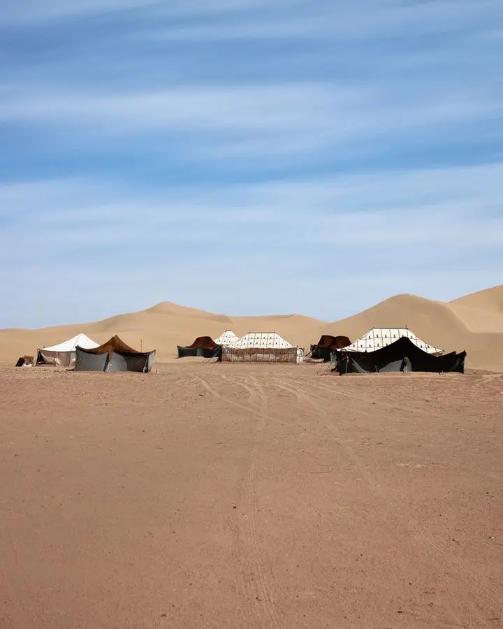 Berber tents in the sandy dunes of M'Hamid El Ghizlane, Morocco under a blue sky.