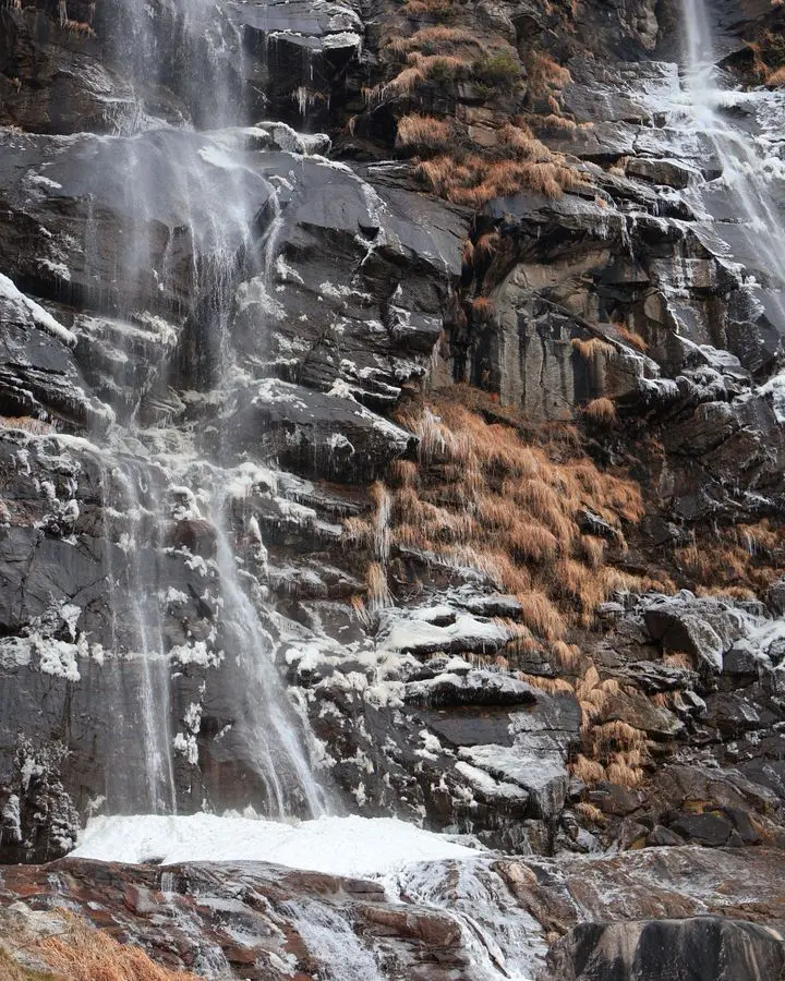 A stunning frozen waterfall cascading down rocky terrain in Chiavenna, Italy, during winter.