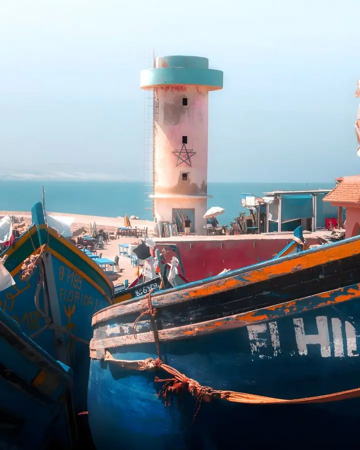Fishing boats docked at Imsouane harbor with a lighthouse, showcasing the coastal charm of Morocco.