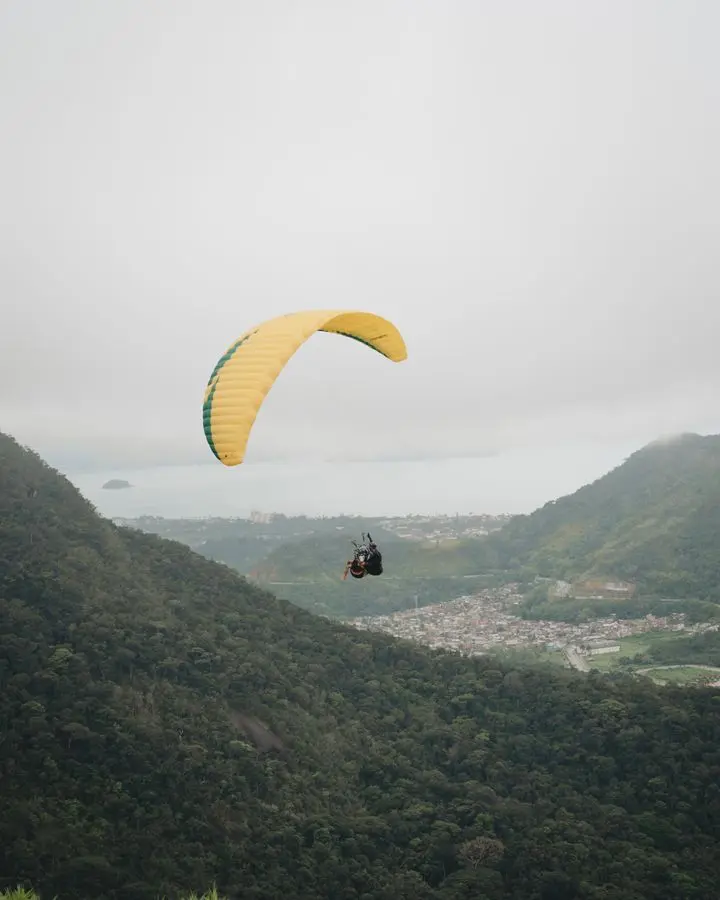 Adventurer enjoys paragliding over a scenic valley on a cloudy day, offering a breathtaking aerial view.