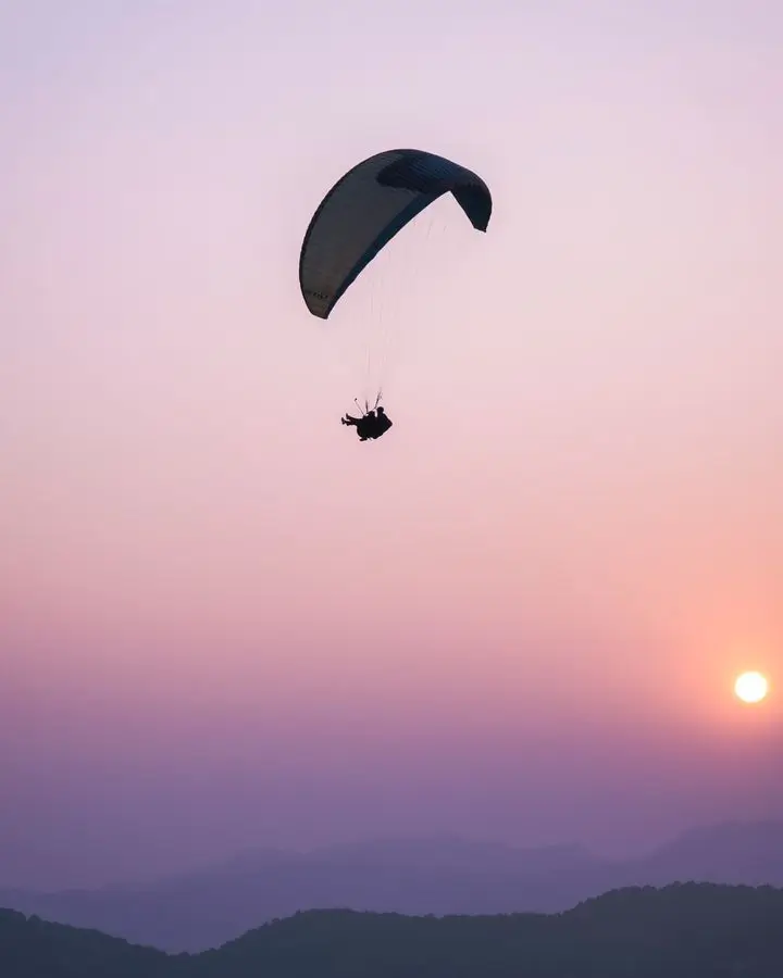 Silhouette of a paraglider soaring against a vibrant sunset over mountains. Adventure and tranquility in harmony.