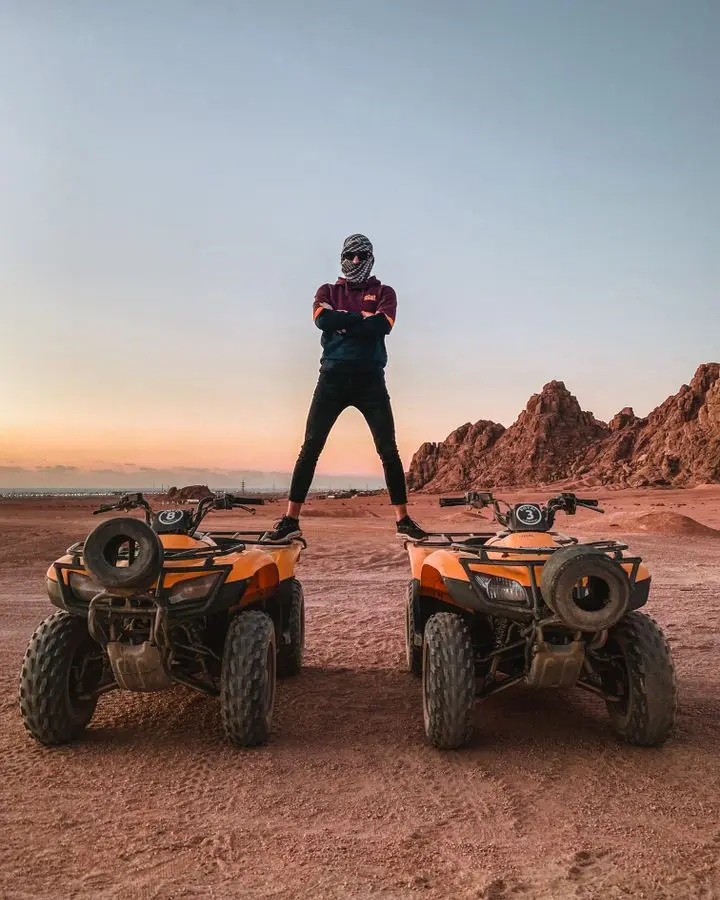 Man on quads with arms crossed, exploring Sinai's desert at sunset.