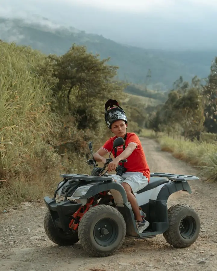 Young boy on ATV on a dirt road in Cáqueza, Colombia with scenic landscape.