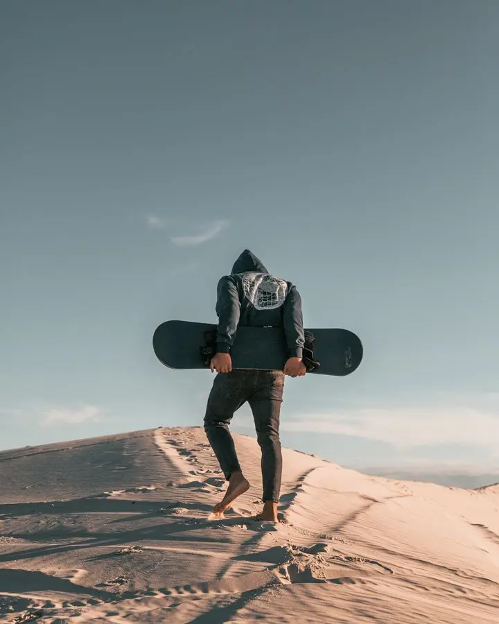 Man with skateboard on desert dune in Cape Town, South Africa. Perfect for adventure and travel themes.
