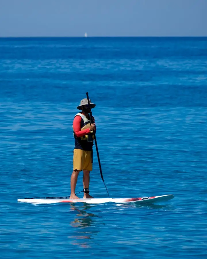 A man enjoying stand-up paddleboarding on the clear blue sea in Perdika, Greece.