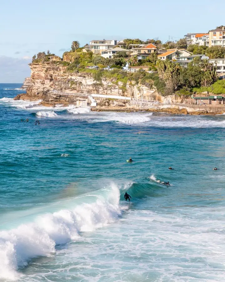 Surfers catch waves near Bondi's scenic cliffs on a bright sunny day.