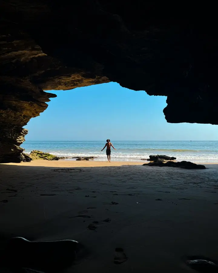 A person silhouetted in a cave opening at a beach in Taghazout, Morocco.