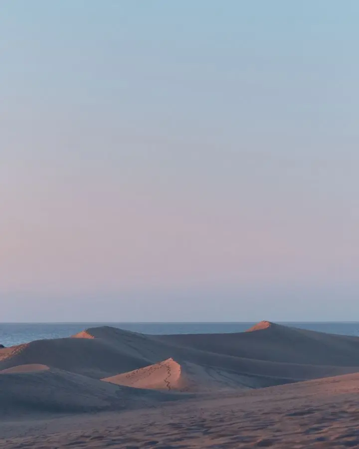 Experience the tranquil beauty of Maspalomas dunes at sunset with soft pastel skies.